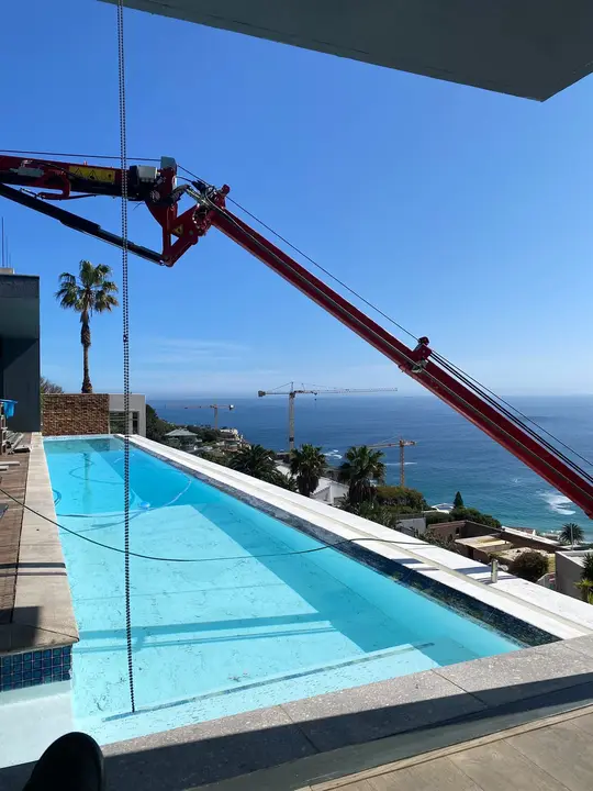 Spider crane lifting glass over a clifftop pool with the Atlantic behind